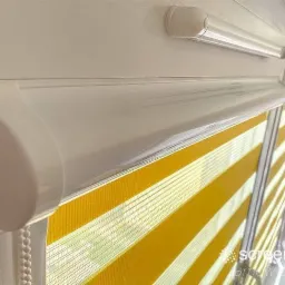 Żółto-białe rolety w kasecie dzień i noc, widoczne z bliska, z delikatnym prześwitem i białym mechanizmem.