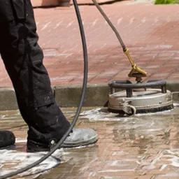 Czyszczenie kostki brukowej na zewnątrz za pomocą myjki ciśnieniowej z obrotową dyszą, widoczne ślady piany i mokra nawierzchnia.