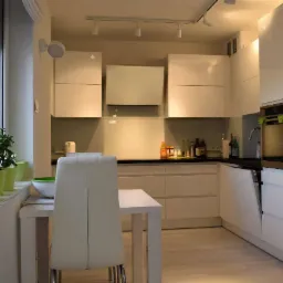 Biała, nowoczesna kuchnia z połyskiem w Pisarzowicach, widok na zabudowę kuchenną z czarnym blatem, stół z krzesłami i roślinami w doniczkach na parapecie.