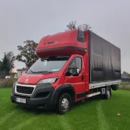 Czerwony samochód dostawczy Peugeot z plandeką na zielonej trawie, widok z przodu, tablice rejestracyjne WI 665HN.