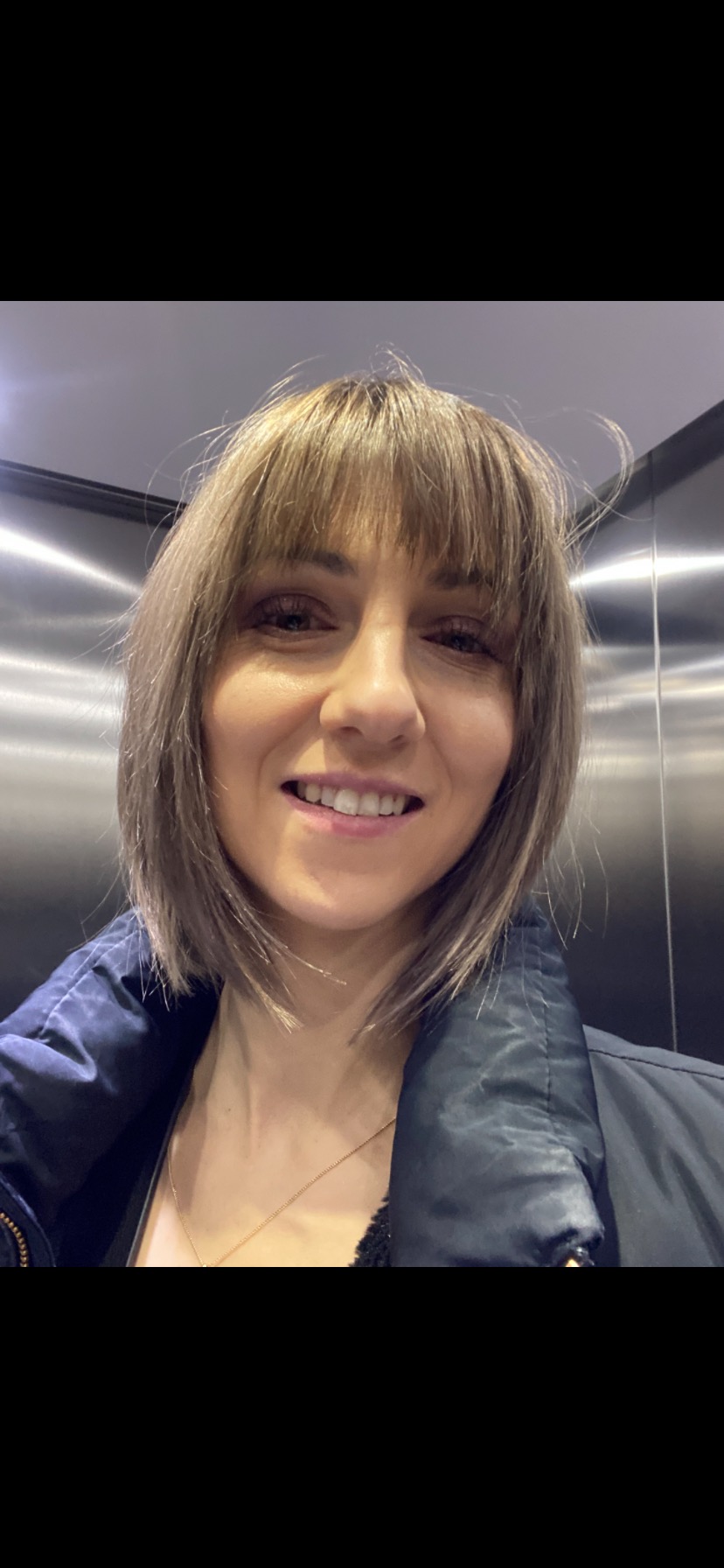 Portret uśmiechniętej kobiety z grzywką i kurtką w windzie.