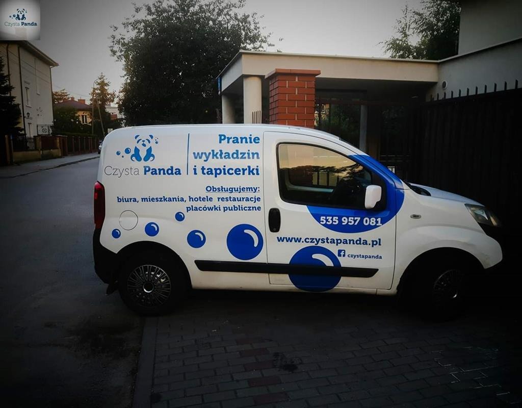 Biała furgonetka z logo firmy 'Czysta Panda' oferującej usługi prania wykładzin i tapicerki, zaparkowana na brukowanej ulicy w dzielnicy domów jednorodzinnych.