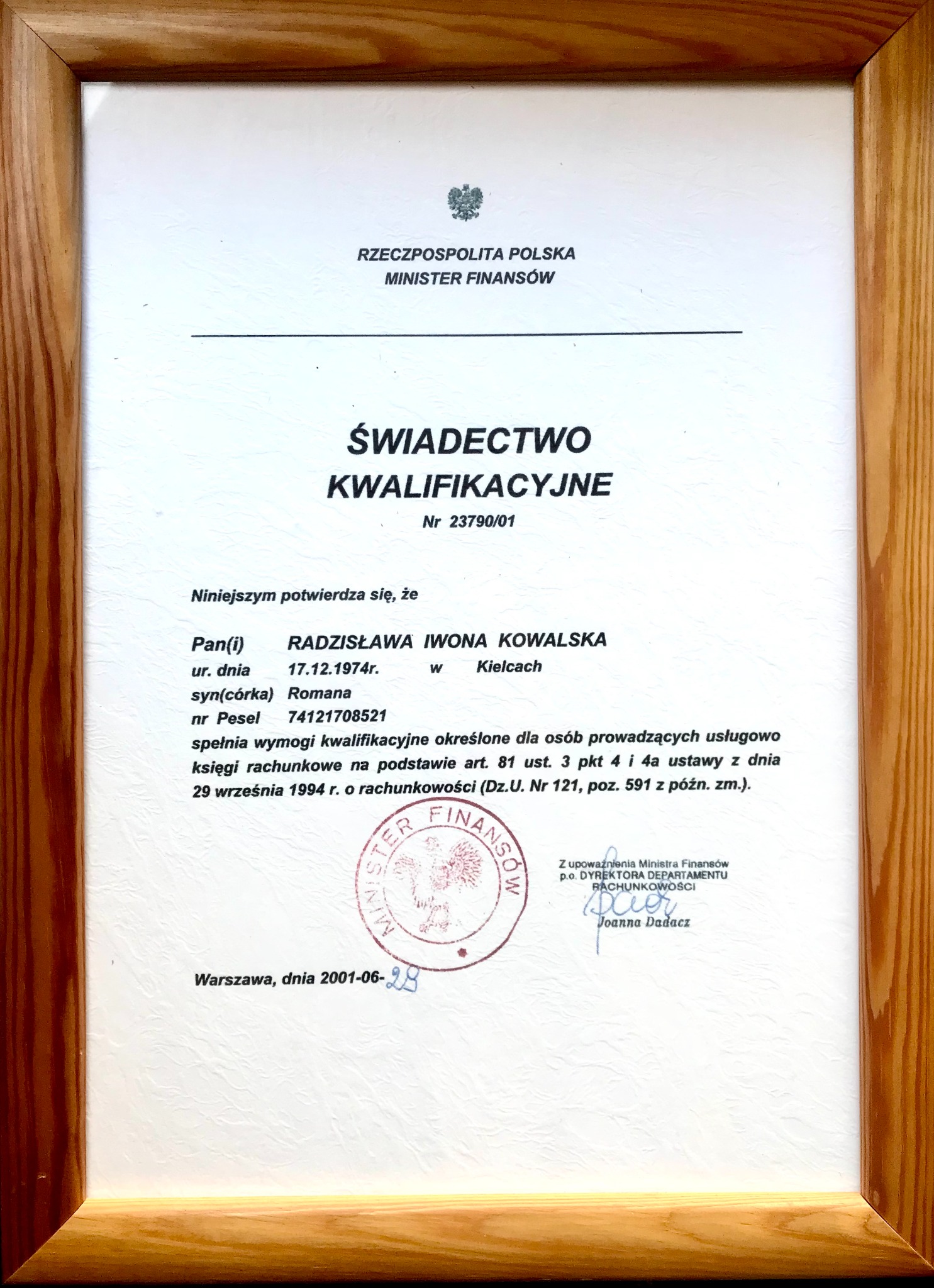 Oprawione w drewnianą ramkę świadectwo kwalifikacyjne Ministerstwa Finansów RP, potwierdzające spełnianie wymogów do usługowego prowadzenia ksiąg rachunkowych przez Radzisławę Iwonę Kowalską.