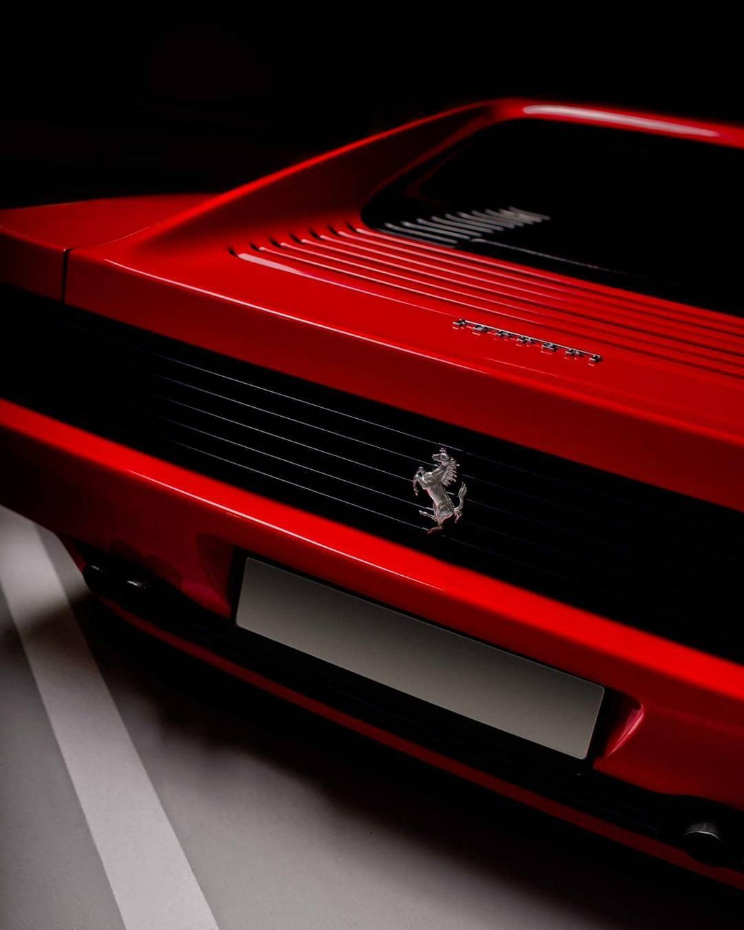 Czerwony Ferrari Testarossa: detal tylnej części z logo, żaluzjami i miejscem na tablicę rejestracyjną w ciemnym otoczeniu.