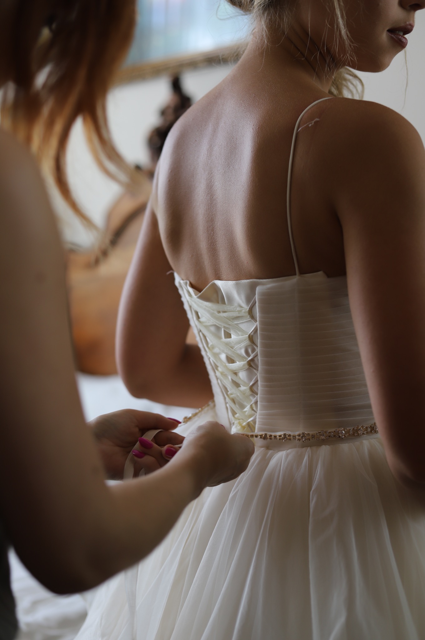 Zapinanie sukni ślubnej z gorsetem i zdobionym paskiem w Szczytnikach, widok z tyłu, delikatne oświetlenie.