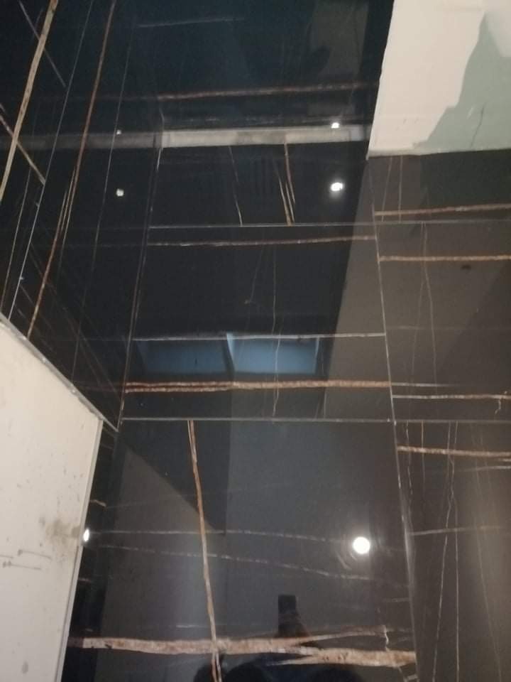 Ściana i podłoga wyłożone czarnymi, błyszczącymi płytkami z brązowymi żyłkami, widoczne niedociągnięcia przy łączeniu z sufitem.