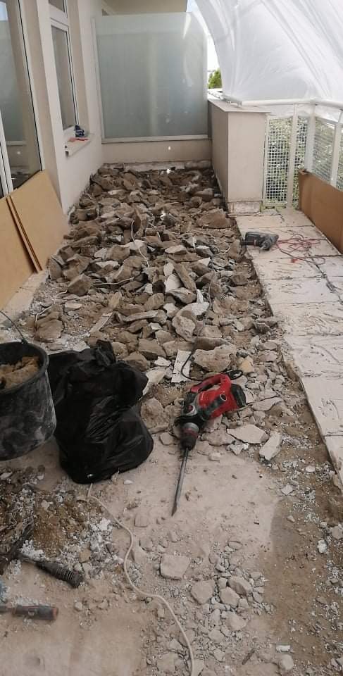 Demontaż starej posadzki na balkonie: gruz, resztki kleju i narzędzia, w tym młot udarowy, widoczne przygotowania do położenia nowej nawierzchni.