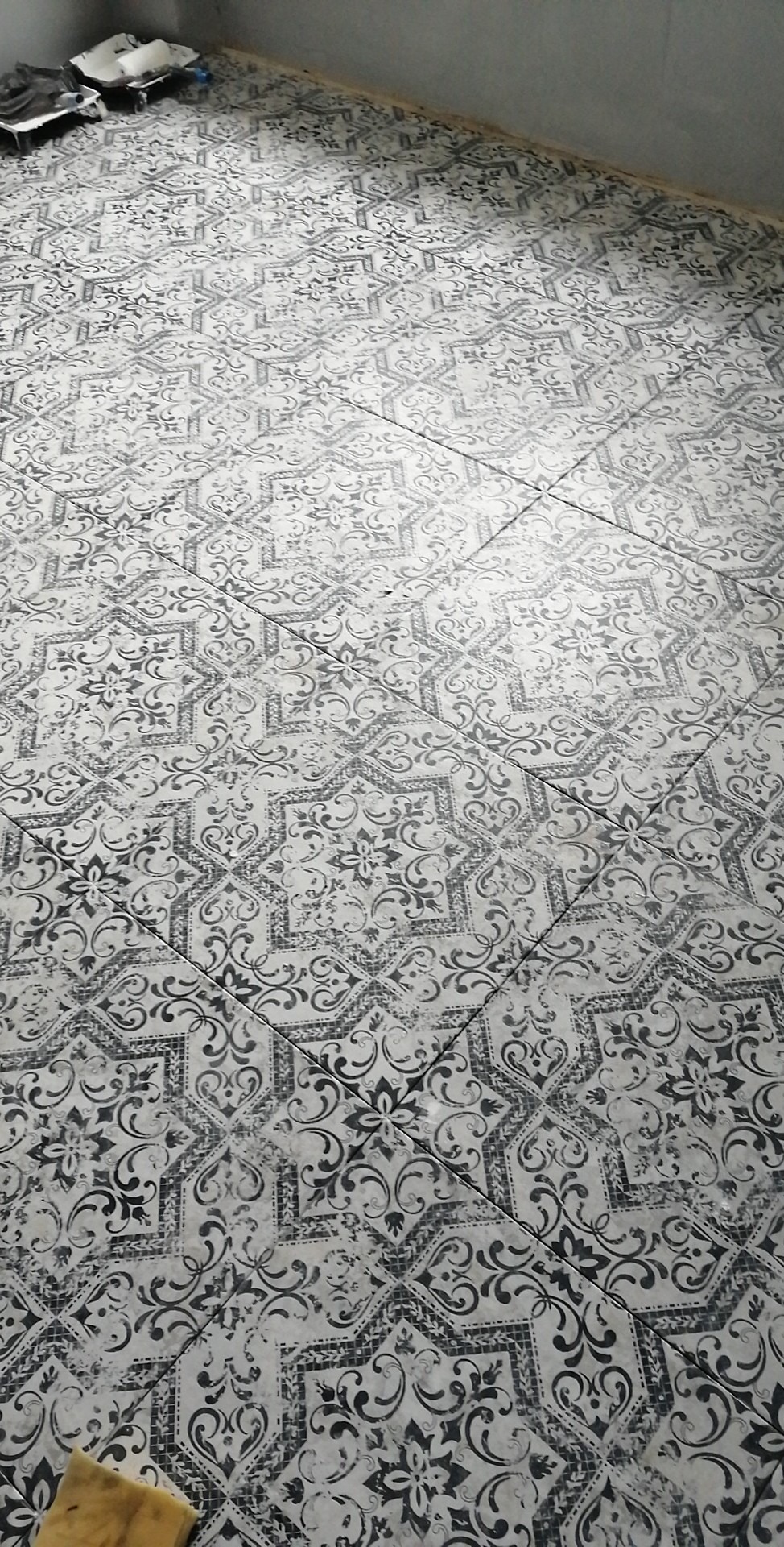 Ułożona podłoga z płytek ceramicznych w stylu vintage, wzór czarno-biały, widoczne narzędzia glazurnicze w tle i w rogu.