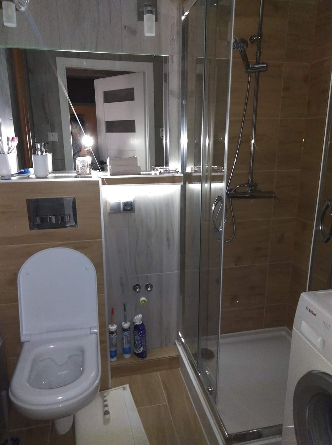 Nowoczesna łazienka po remoncie z kabiną prysznicową, podświetlanym lustrem, wiszącą toaletą i widocznymi silikonami montażowymi.