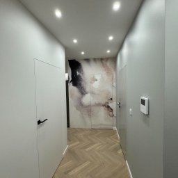 Nowoczesny korytarz z parkietem w jodełkę, ukrytymi drzwiami i abstrakcyjną tapetą w odcieniach beżu i czerni. Minimalistyczny design, oświetlenie punktowe.