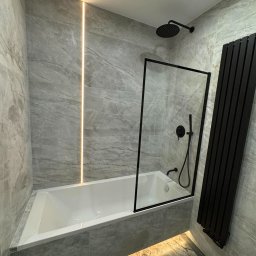 POL-UK REMONT EXPERT - Nowoczesna łazienka z szarymi płytkami imitującymi marmur, podświetlana listwa LED i czarna armatura. Minimalistyczny design z wanną i grzejnikiem.