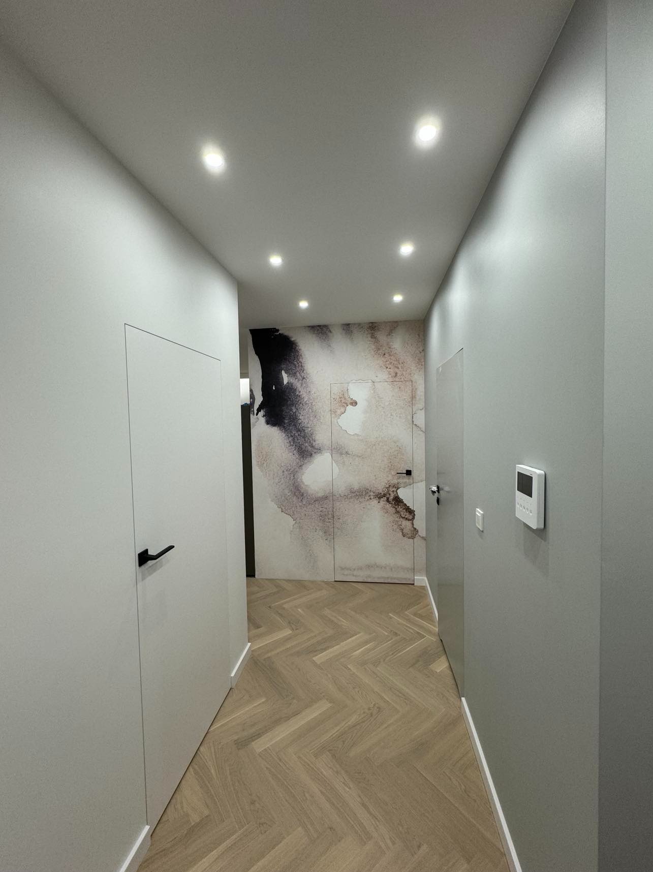 Nowoczesny korytarz z parkietem w jodełkę, ukrytymi drzwiami i abstrakcyjną tapetą w odcieniach beżu i czerni. Minimalistyczny design, oświetlenie punktowe.