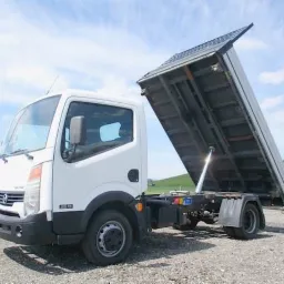 Biała wywrotka z podniesioną skrzynią ładunkową na tle zielonego pola i błękitnego nieba z chmurami.