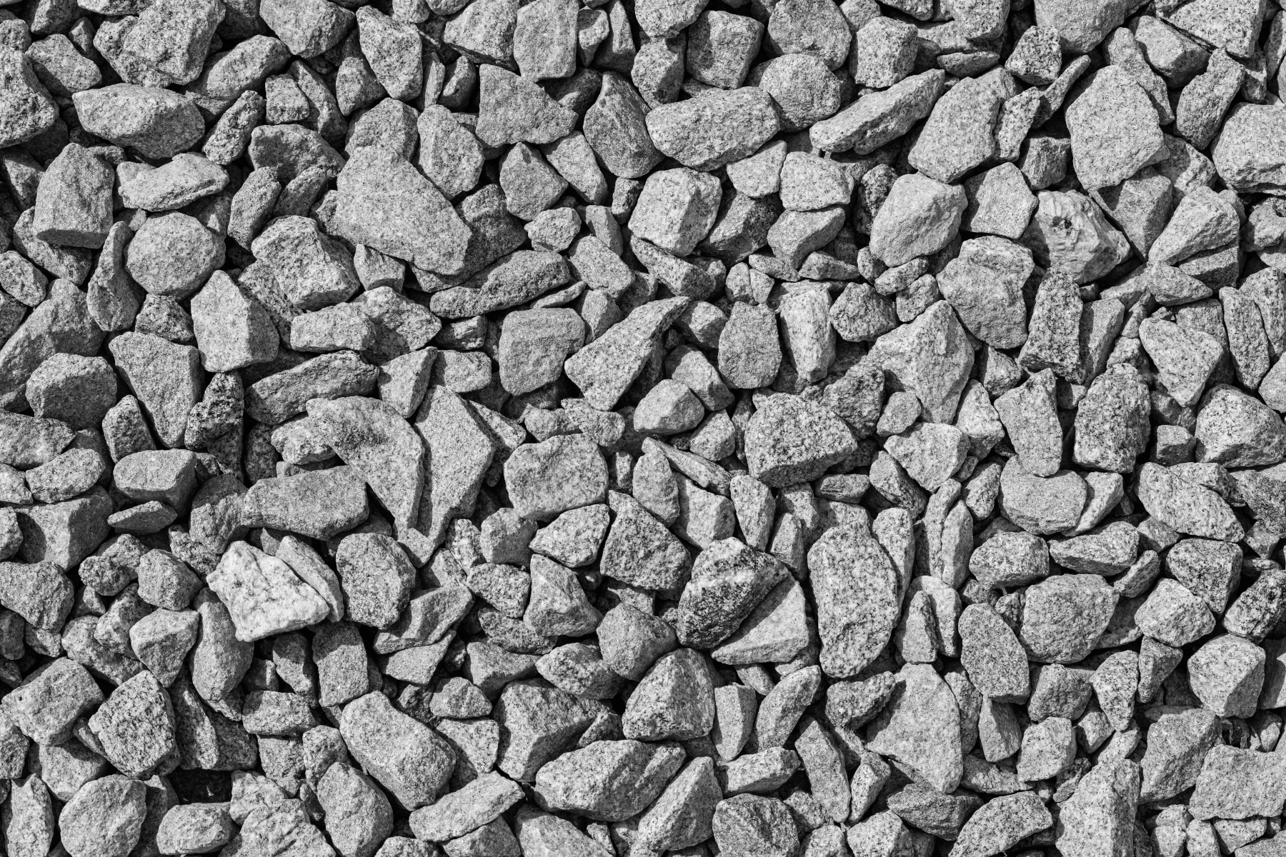 Szary, drobny kamień o nieregularnych kształtach wypełniający całą powierzchnię kadru, oświetlony z góry, tworzący teksturę.