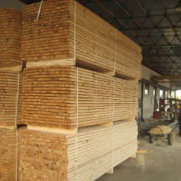 Stosy świeżo przetartej tarcicy sosnowej składowane w hali, widoczni pracownicy oraz wózek transportowy