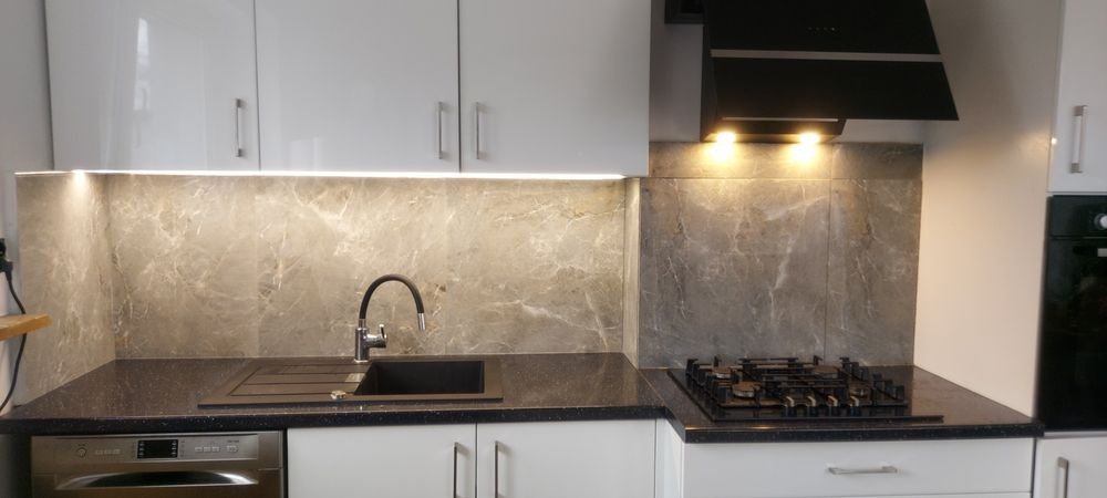 Wykończona kuchnia z marmurowym backsplashiem, czarnym zlewozmywakiem i płytą gazową, oświetleniem LED pod szafkami i białymi frontami szafek.