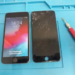 Smartfon z działającym ekranem obok smartfona z pękniętym ekranem, leżące na niebieskiej macie do napraw, obok czerwony śrubokręt precyzyjny.