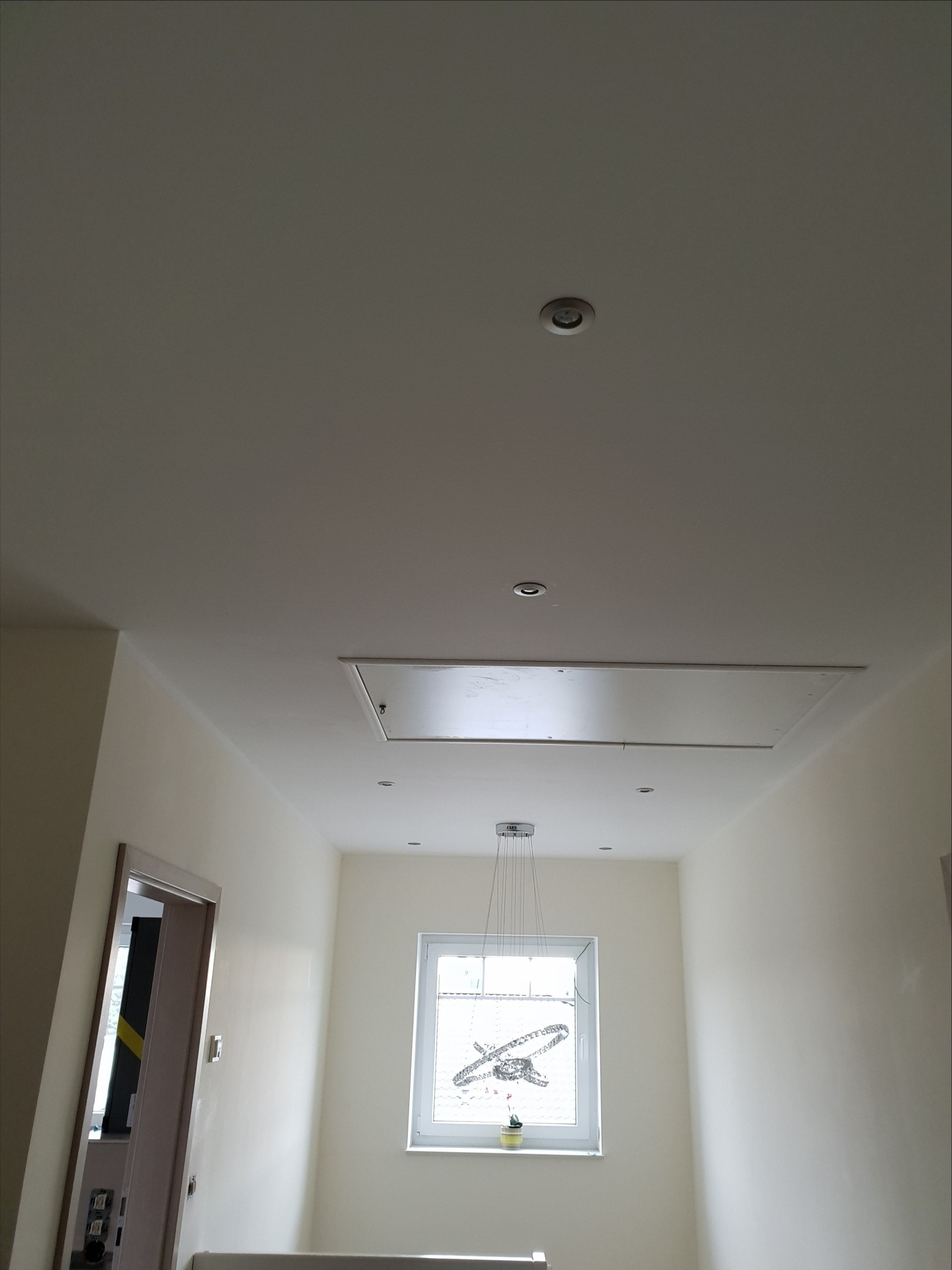 Korytarz z białymi ścianami, oświetleniem punktowym w suficie i nowoczesną lampą wiszącą przy oknie.