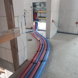 Usługi hydrauliczne - Rozprowadzenie rur instalacji ogrzewania podłogowego w izolacji, widoczne kolektory w szafce, ściany z betonu komórkowego w surowym stanie.