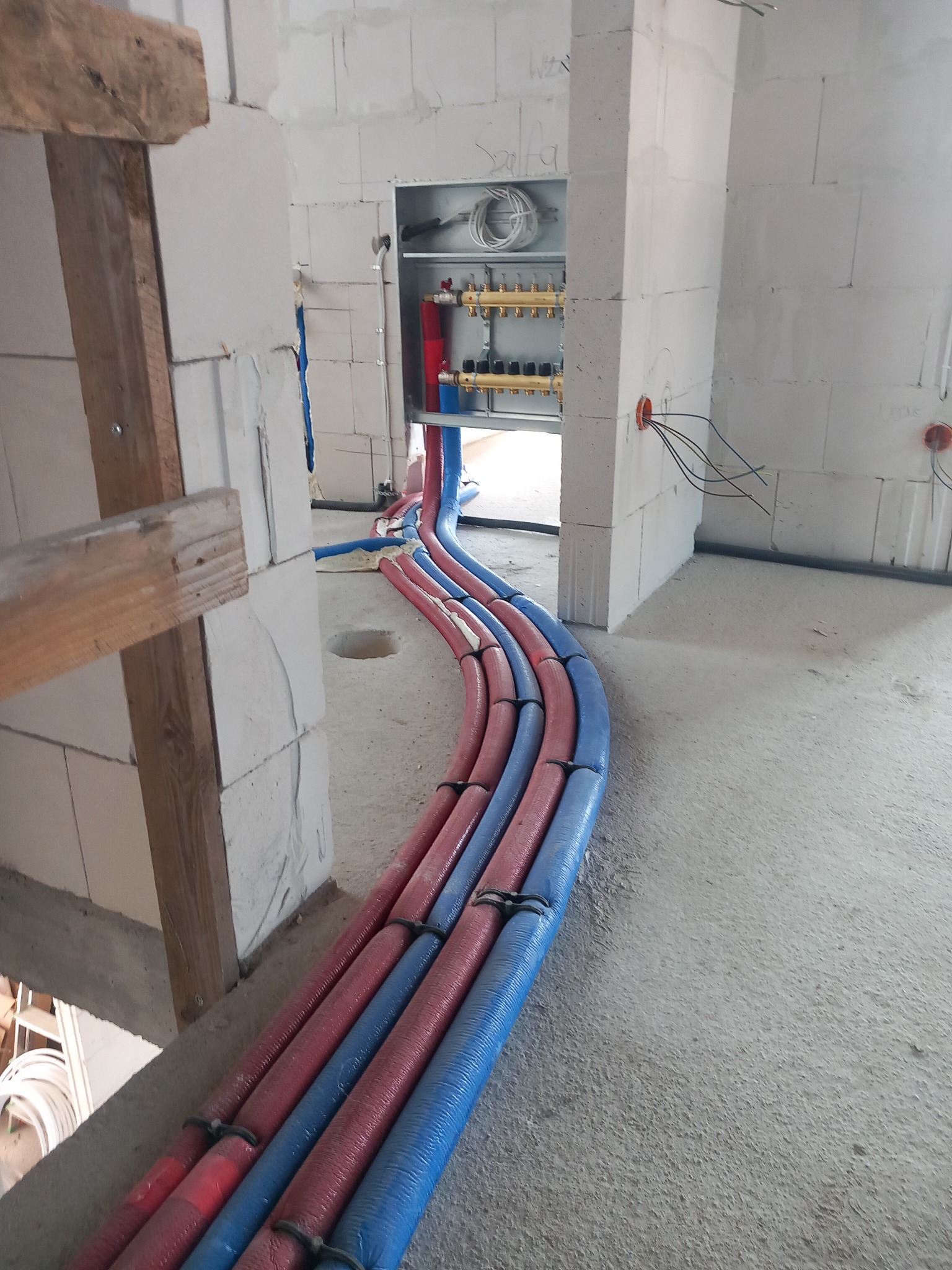 Rozprowadzenie rur instalacji ogrzewania podłogowego w izolacji, widoczne kolektory w szafce, ściany z betonu komórkowego w surowym stanie.