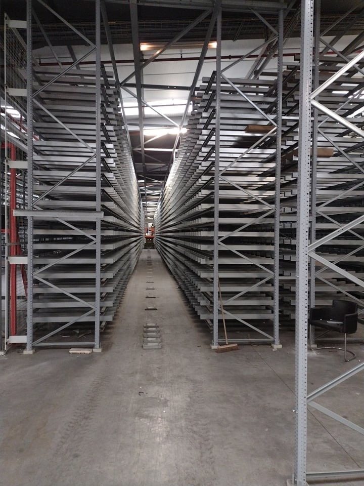 Długi korytarz między rzędami pustych, metalowych regałów magazynowych w hali w Rzeszowie, widok w głąb magazynu, na podłodze widoczne ślady użytkowania i szczotka.