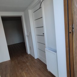 Yaroslav Zakhidnyy - Wnętrze mieszkania w trakcie wykańczania: drewnopodobne panele podłogowe, białe ściany, grzejnik i białe drzwi z poziomymi przeszkleniami, widoczne kable wystające ze ściany.