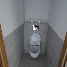 Yaroslav Zakhidnyy - Wąska toaleta po remoncie, wykończona szarymi płytkami imitującymi drewno, z podwieszaną muszlą klozetową i minimalistycznym panelem sterującym spłukiwaniem.