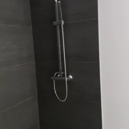 Nowoczesna kabina prysznicowa z czarnymi płytkami imitującymi kamień i chromowaną armaturą, deszczownica kwadratowa, minimalistyczny design.