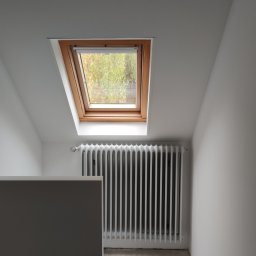 Yaroslav Zakhidnyy - Poddasze po remoncie, widoczne białe ściany, okno dachowe z drewnianą ramą, grzejnik pomalowany na biało i surowa betonowa posadzka przed położeniem wykończenia.