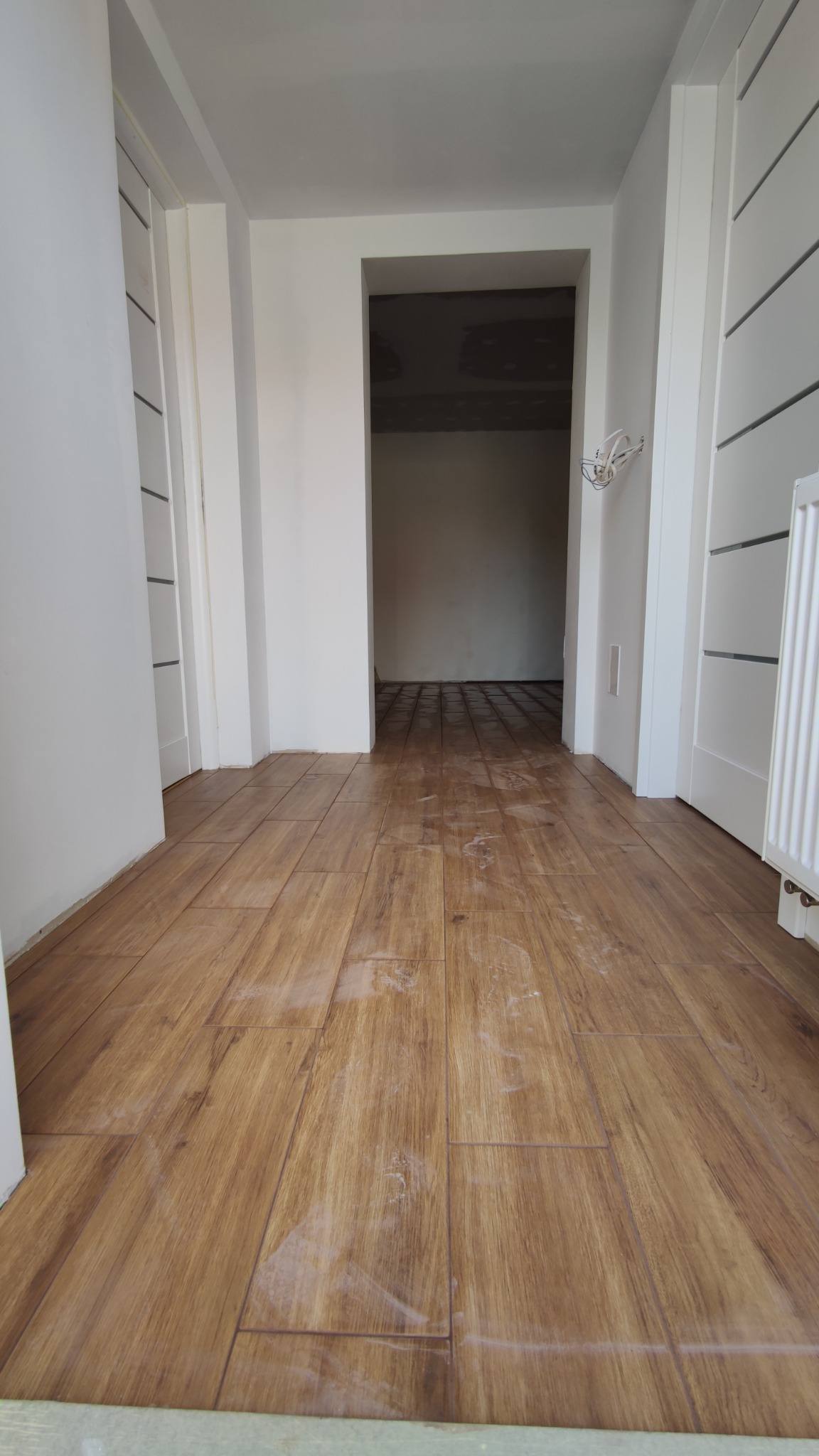 Ułożona podłoga z płytek imitujących drewno w jasnym korytarzu, widoczne ślady po fugowaniu i drobne zabrudzenia na powierzchni.