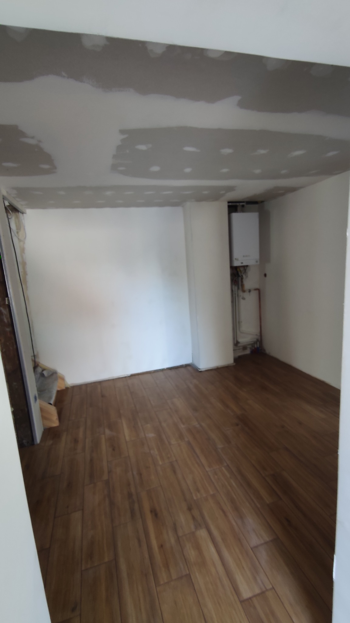 Pokój po remoncie: panele podłogowe imitujące drewno, ściany przygotowane do malowania, widoczny piec gazowy w rogu pomieszczenia.