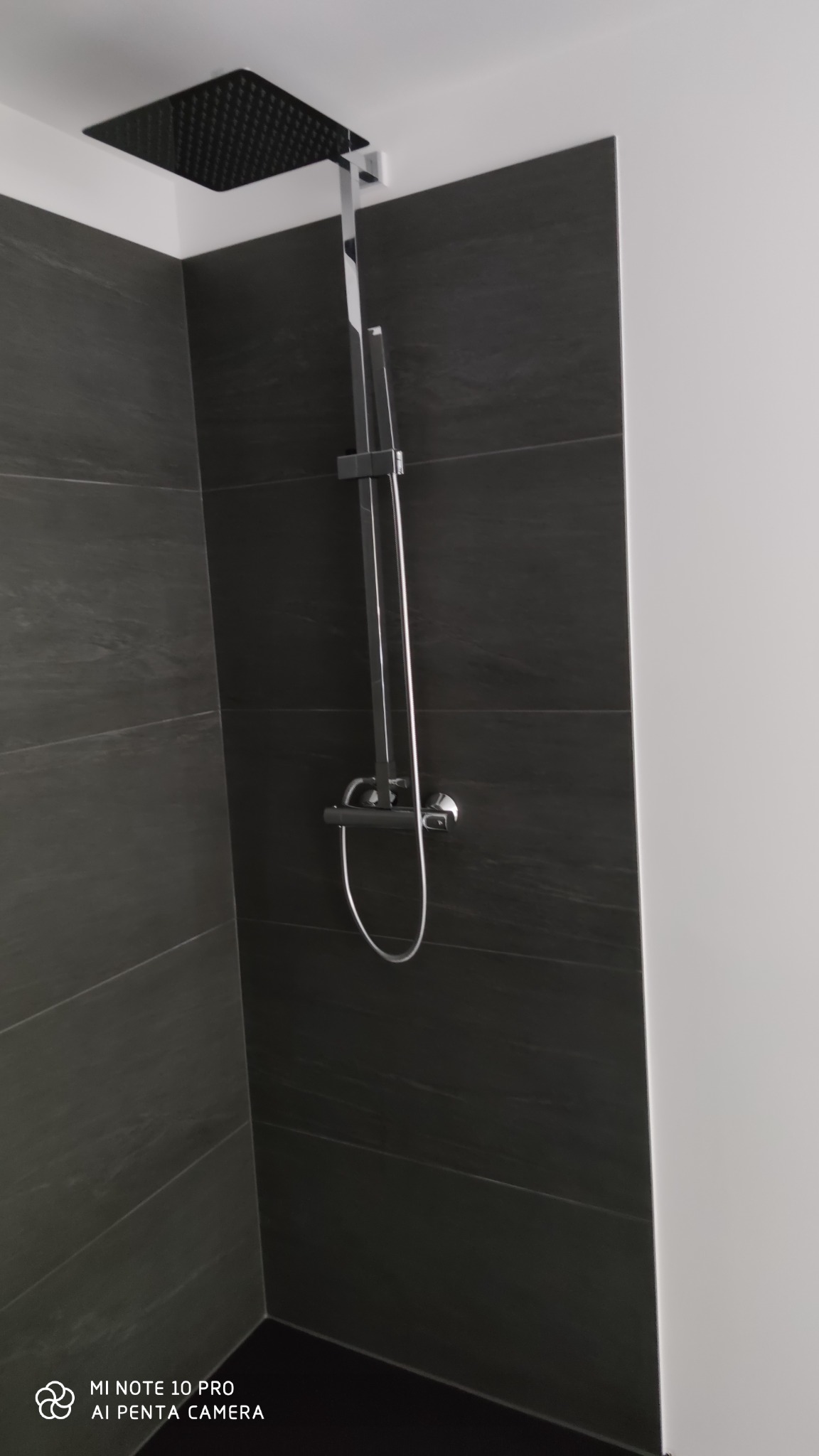 Nowoczesna kabina prysznicowa z czarnymi płytkami imitującymi kamień i chromowaną armaturą, deszczownica kwadratowa, minimalistyczny design.