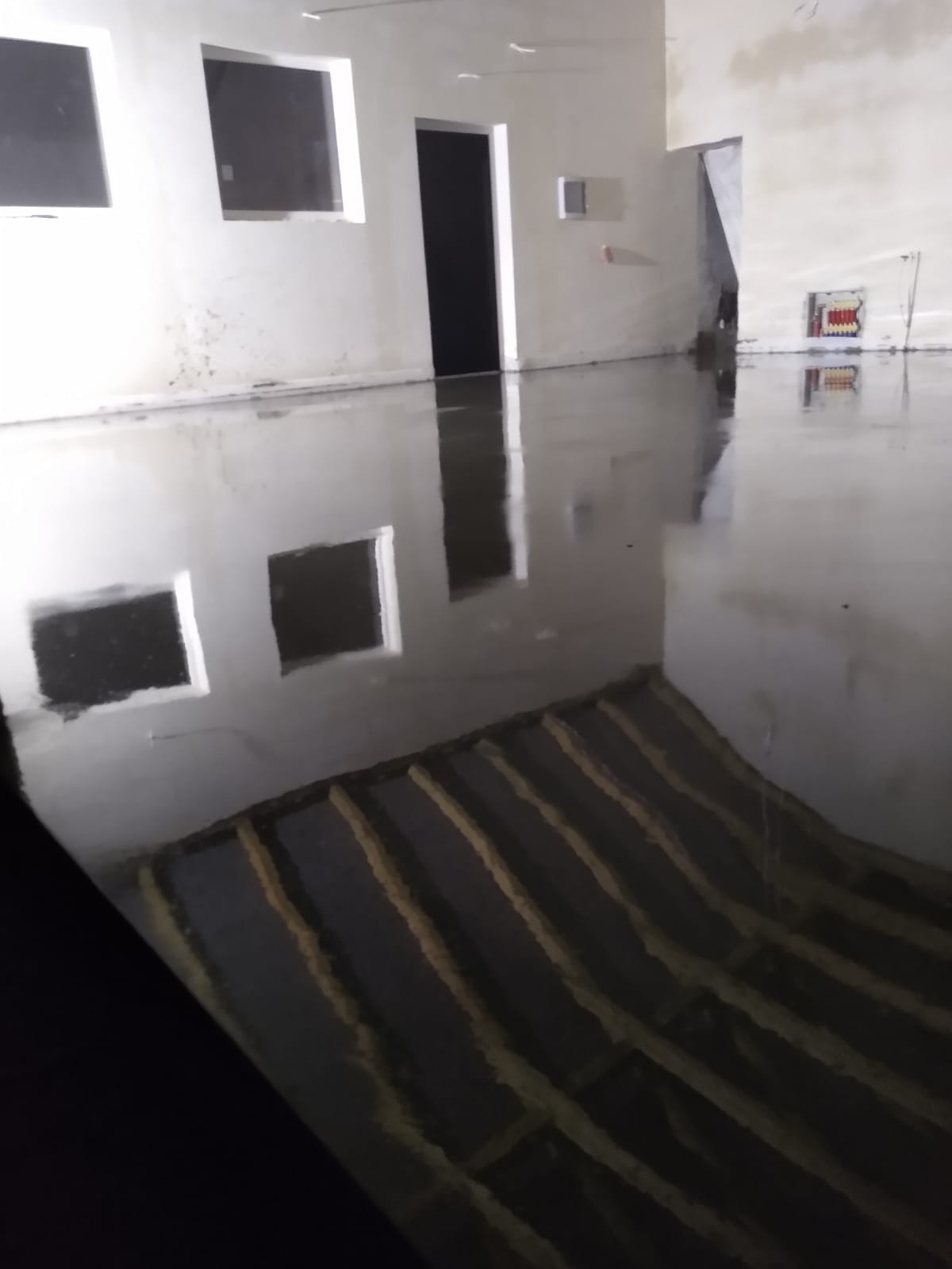 Świeżo wylana, mokra posadzka jastrychowa w surowym wnętrzu z widocznymi elementami ogrzewania podłogowego i odbiciami okien.