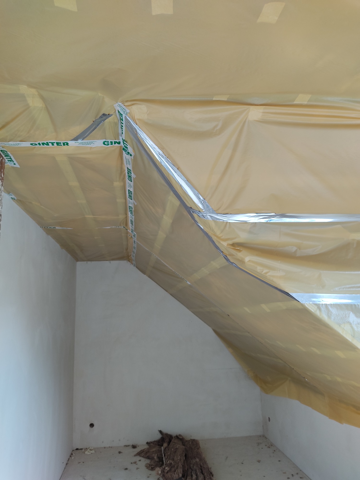 Przygotowanie pomieszczenia do prac wykończeniowych; folia ochronna przymocowana taśmą do ścian i sufitu, widoczne fragmenty izolacji na podłodze.