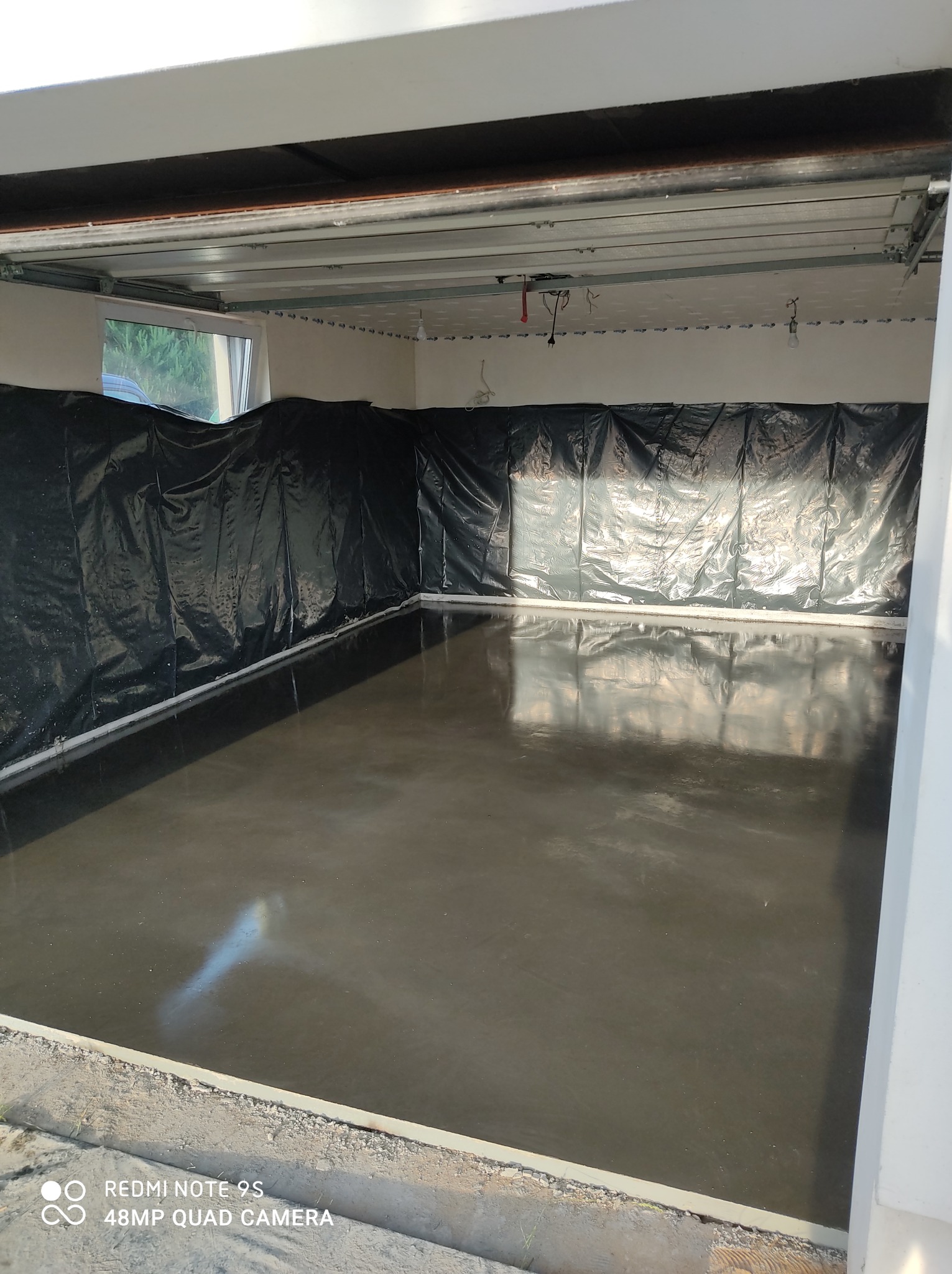 Świeżo wylana, gładka posadzka w pomieszczeniu z zabezpieczonymi ścianami folią, widoczne elementy konstrukcji sufitu.