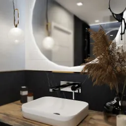Nowoczesna łazienka z umywalką nablatową, okrągłym lustrem z podświetleniem, czarnym marmurem na ścianach i dekoracyjną lampą wiszącą.