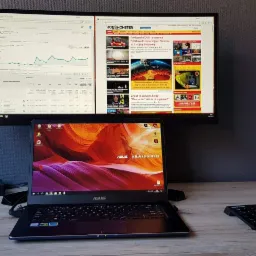 Stanowisko pracy z laptopem Asus i dwoma monitorami wyświetlającymi dane analityczne strony internetowej oraz artykuły z portalu informacyjnego.