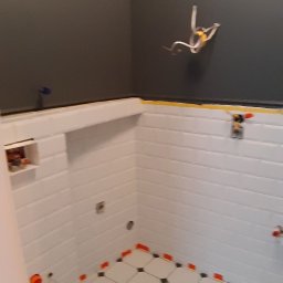 Vitalii - Łazienka w trakcie remontu: białe, poziome płytki ścienne z fugą, czarno-biała podłoga w romby z pomarańczowymi krzyżykami dystansowymi, instalacja elektryczna wystająca ze ściany, szara ściana...