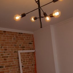 Vitalii - Czarna, nowoczesna lampa sufitowa z sześcioma żarówkami edisona, zamontowana w pomieszczeniu z częściowo odsłoniętą ścianą z czerwonej cegły i białymi ścianami, widoczne przygotowania do prac...
