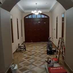 Vitalii - Korytarz z nową, wzorzystą podłogą z płytek, narzędzia glazurnicze i drabina w tle, ściany pomalowane na jasny kolor, widoczne elementy oświetlenia sufitowego.