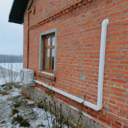 Zewnętrzna jednostka klimatyzacji Panasonic Etherea zamontowana na ścianie budynku z czerwonej cegły, widoczna instalacja odprowadzająca skropliny w białej rurze PCV.