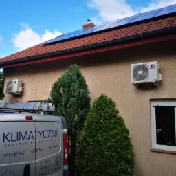 Dwa klimatyzatory Gree zamontowane na elewacji domu jednorodzinnego z panelami słonecznymi na dachu; drabina na dachu srebrnego samochodu serwisowego z napisem 'Klimatyczni' częściowo zasłania widok.