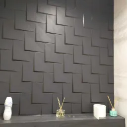 Grafitowa ściana z trójwymiarowych, kwadratowych paneli w łazience, z dekoracjami zapachowymi na półce poniżej.