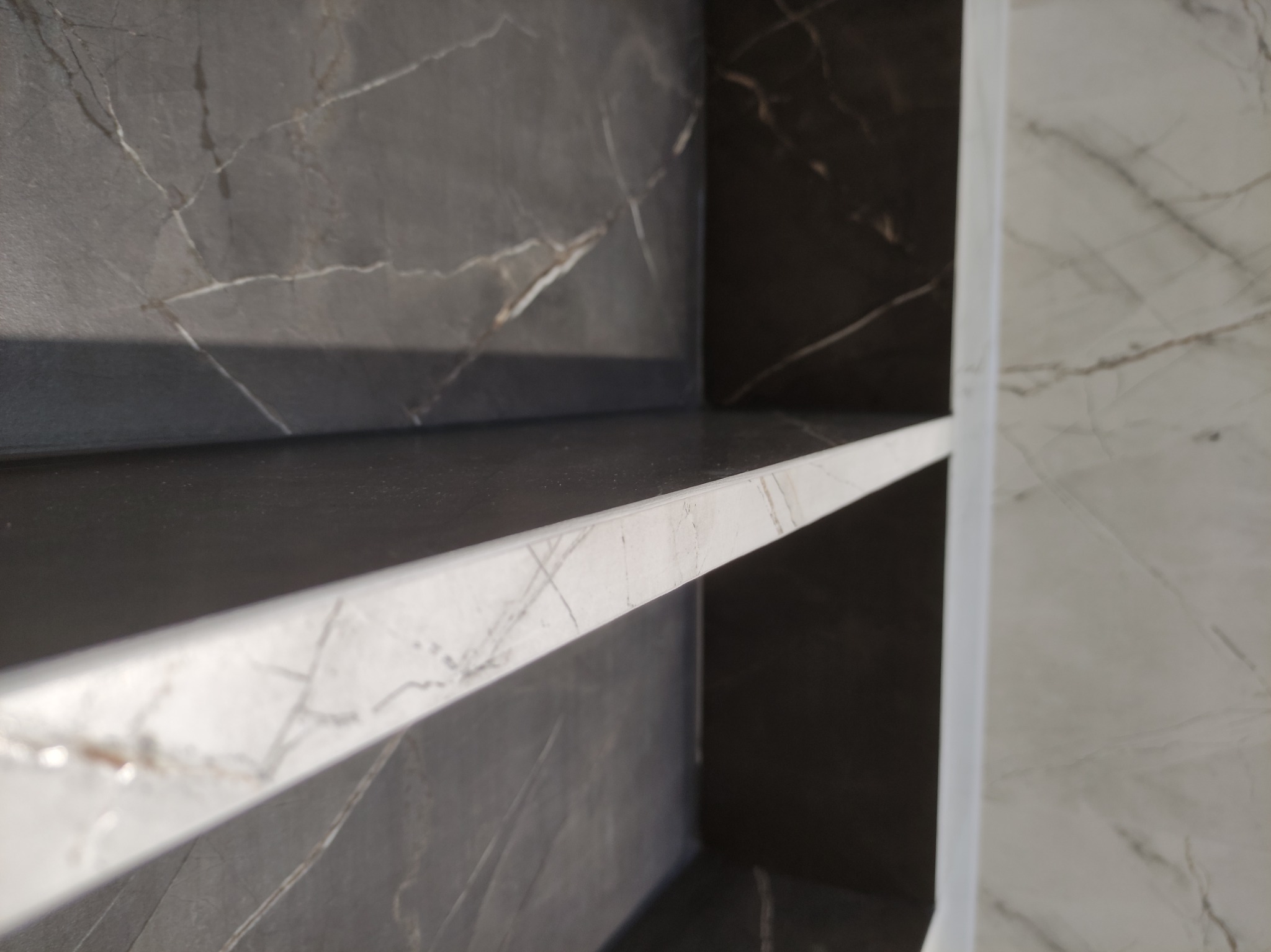 Półka wnękowa wykończona płytkami imitującymi ciemny marmur z jasnymi żyłami, z widoczną krawędzią wykończeniową w kolorze białym.