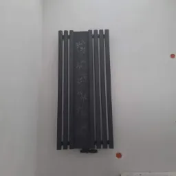 Czarny, dekoracyjny grzejnik panelowy z motywem kwiatowym zamontowany na białej ścianie w surowym wnętrzu.