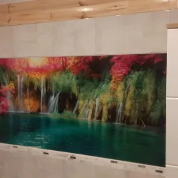 Grafika z motywem wodospadu wklejona między szare płytki w łazience, nad nią drewniana listwa podsufitowa, obok biała szafka łazienkowa.