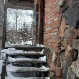 Schody wejściowe do domu w Ełku, pokryte śniegiem, z kamienną i ceglaną elewacją.