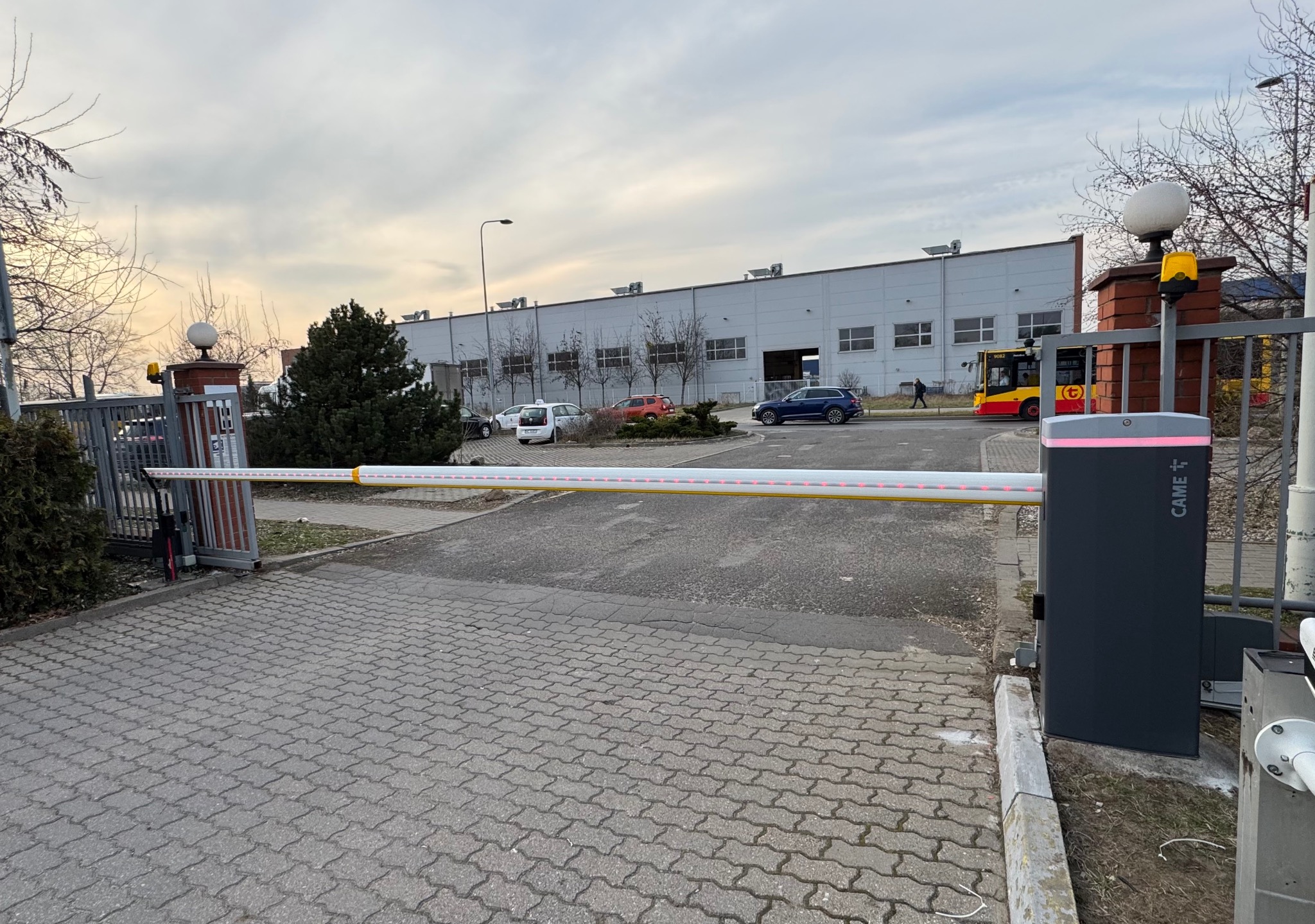 Automatyczna bariera wjazdowa CAME z sygnalizacją świetlną, zainstalowana na posesji w Warszawie. Widoczny budynek w tle i kostka brukowa na podjeździe.