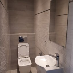 F.H.U. PYRAMID JacekPyra - Nowoczesna łazienka po remoncie, z wiszącą toaletą z podtynkową spłuczką, umywalką na szafce i dużym lustrem, wykończona płytkami w odcieniach szarości z delikatnym wzorem.