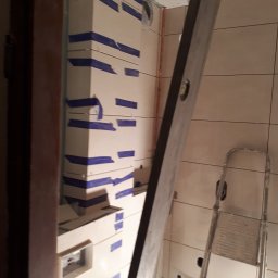 F.H.U. PYRAMID JacekPyra - W trakcie zabudowy pionu wentylacyjnego płytami kartonowo-gipsowymi w łazience, zabezpieczonymi taśmą malarską, widoczna poziomica i drabina.